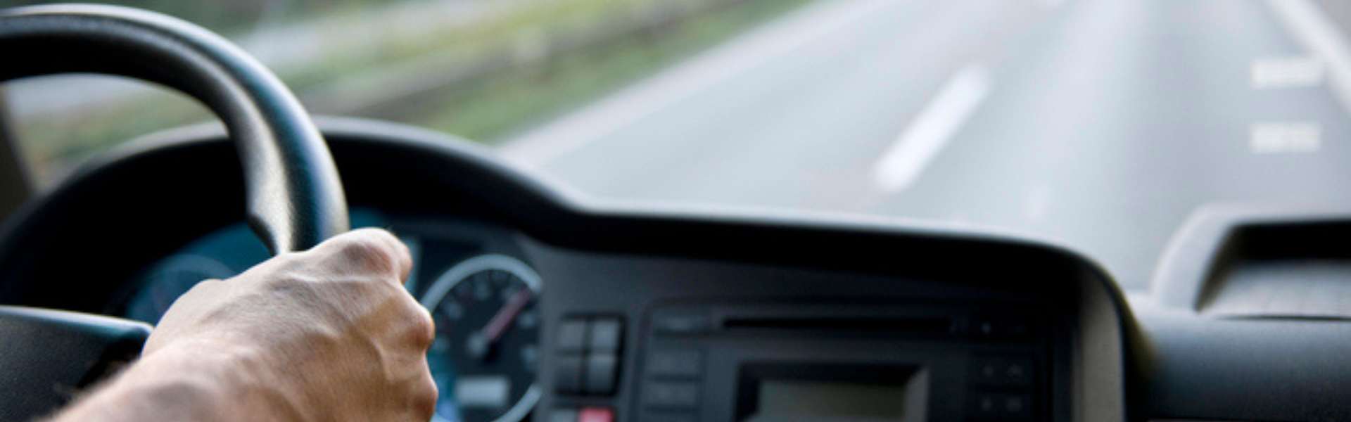 man at the wheel of a semi truck looking out of the cab at the road ahead