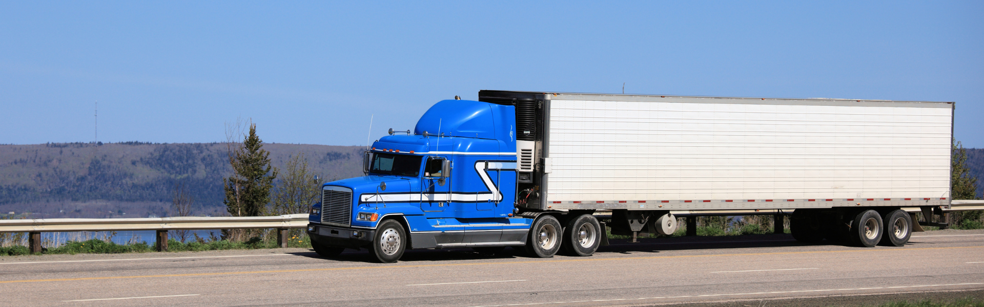 blue semi truck with white trailer on scenic road