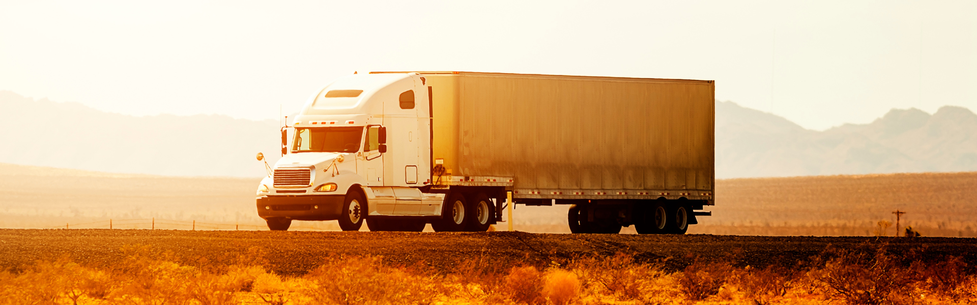 semi truck in the glow of sunset parked on pavement with mountains in the back ground