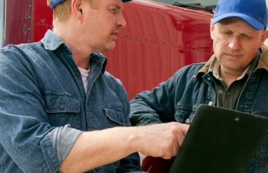 two men looking at clipboard in front of semi truck