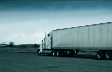 white semi truck pulling white trailer in rural area driving away from camera