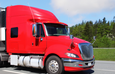 red semi truck with white trailer parked on roadside with green trees in the background.