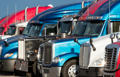 Variety of semi trucks in many different colors, makes, and years parked in a row.