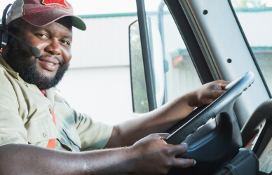 black man wearing ball cap in the cab at the wheel of semi truck