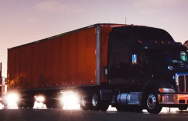 Truck sitting in a truck stop as the sun goes down in the distance. A chain of large big rig trucks one after another.
